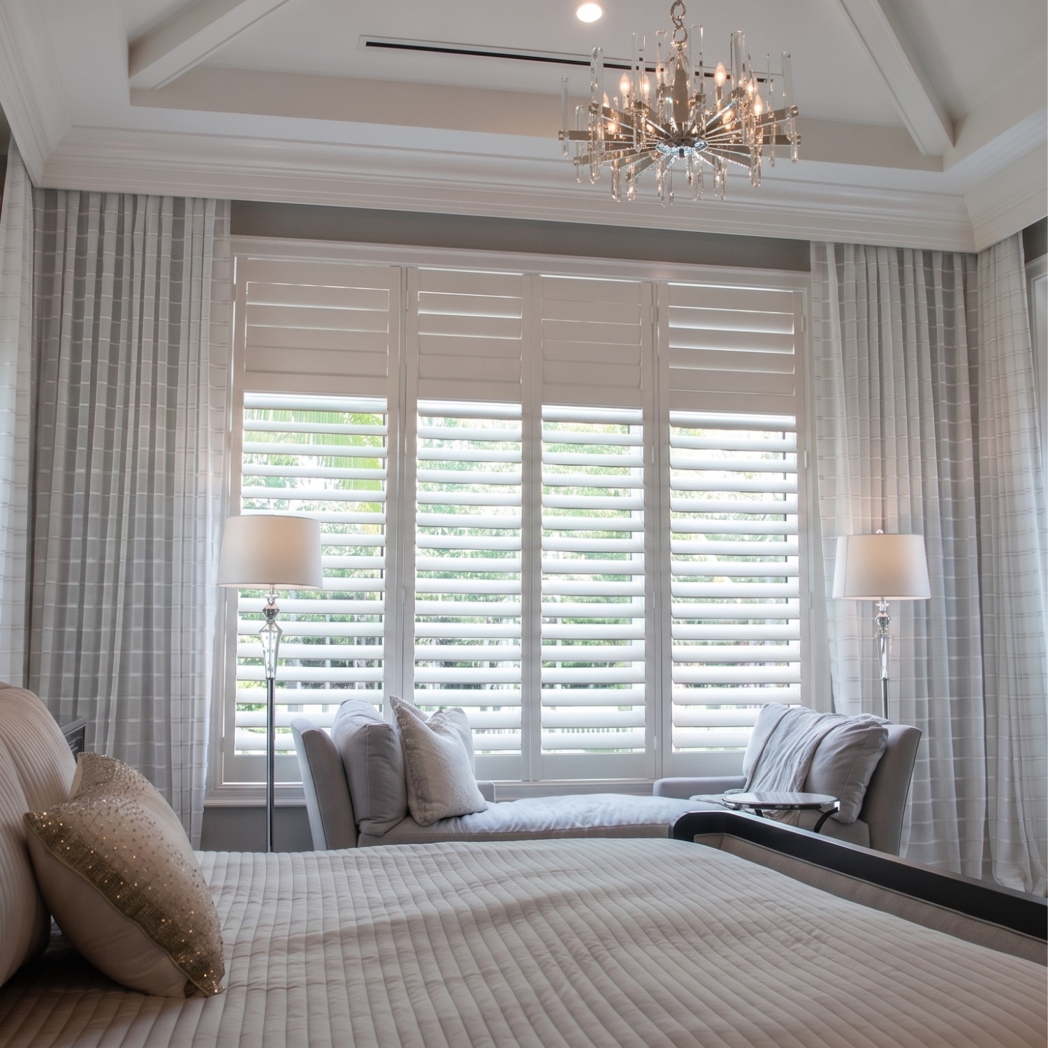 White hardwood plantation shutters in an elegant Naples master bedroom with chandelier and window seat