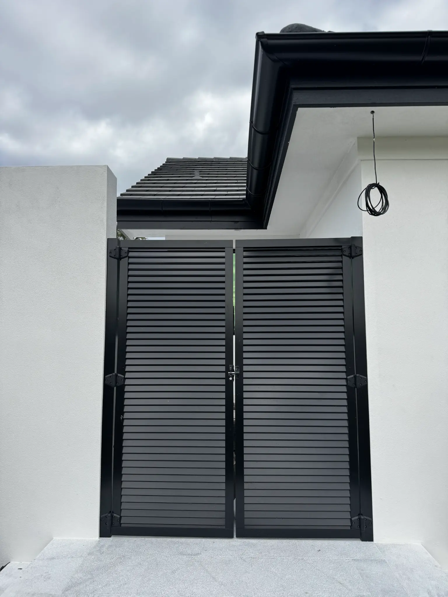 Black double louvered gates between stucco walls