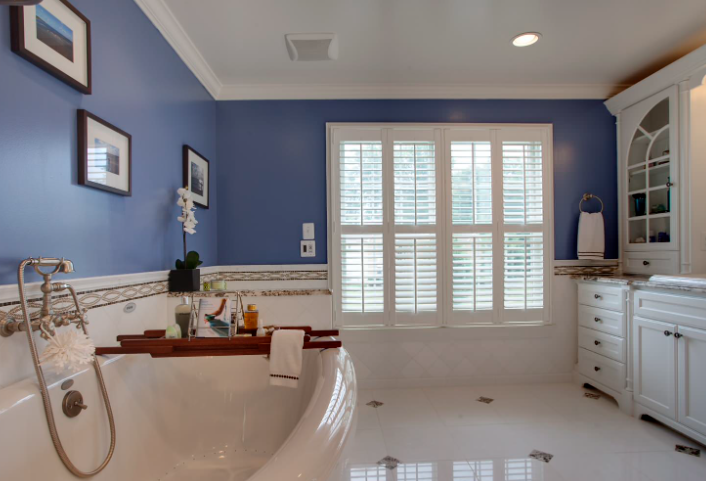 White plantation shutters in a Naples bathroom with blue walls and freestanding soaking tub