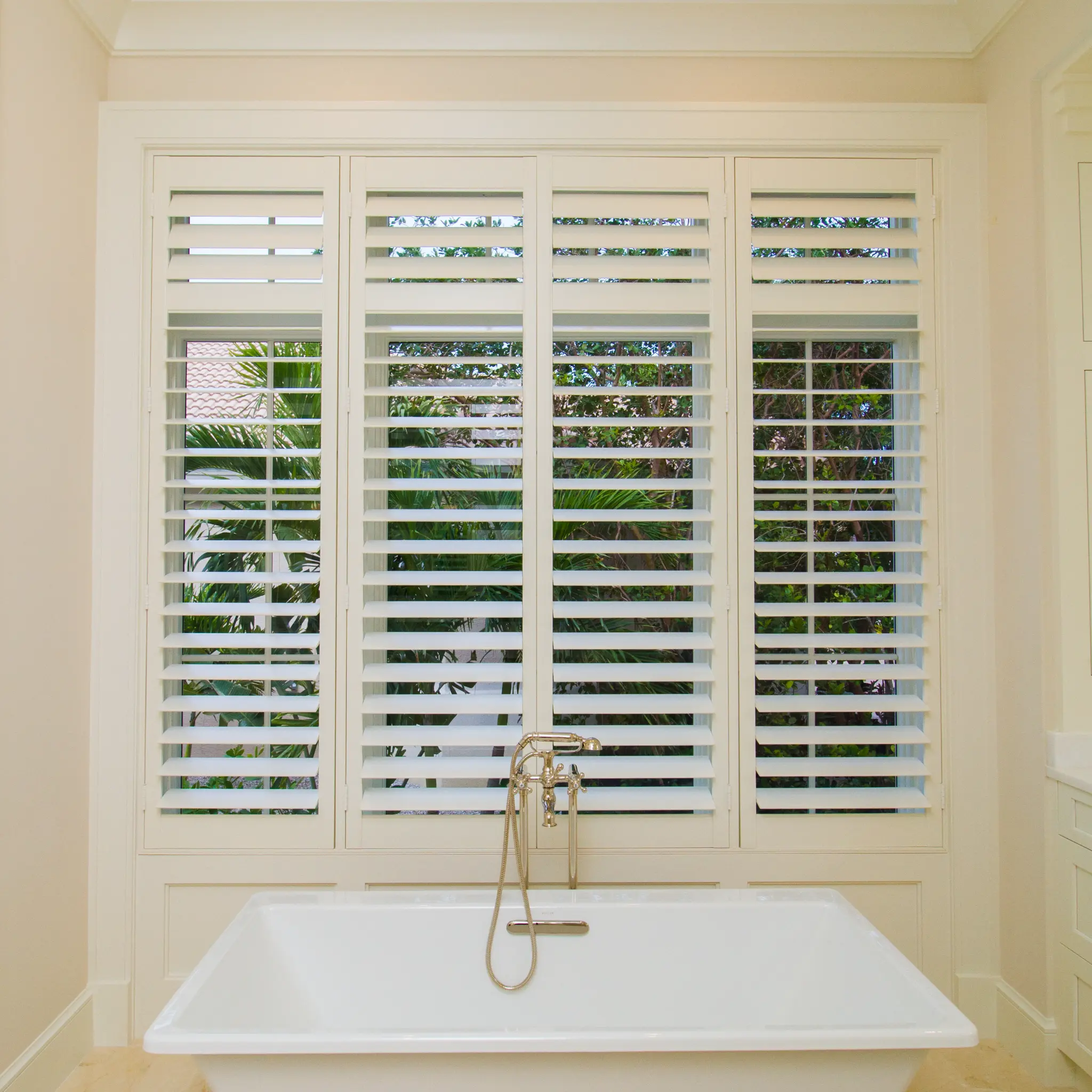 White plantation shutters with open louvers above a freestanding bathtub in a bright Naples bathroom