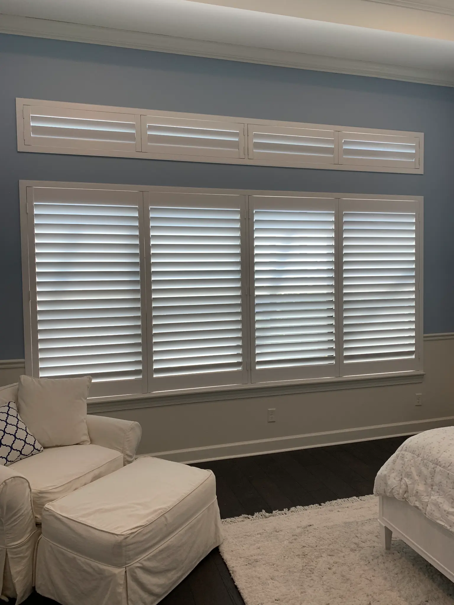 White plantation shutters with transom panels installed in a Naples bedroom with blue-grey walls