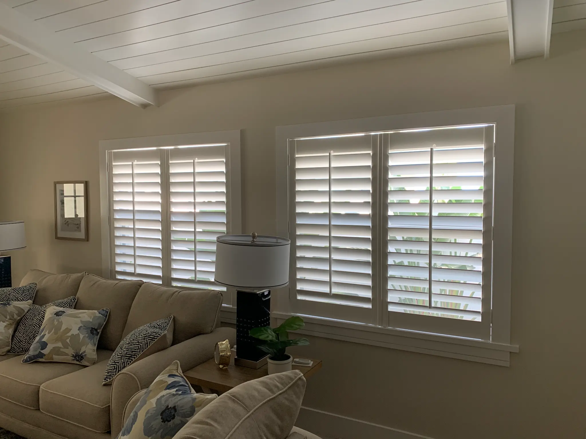 White plantation shutters installed across two large windows in a Naples living room with shiplap ceiling