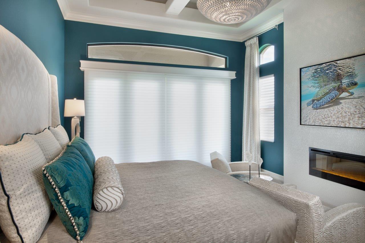 White fabric shades across bedroom windows beside a bed